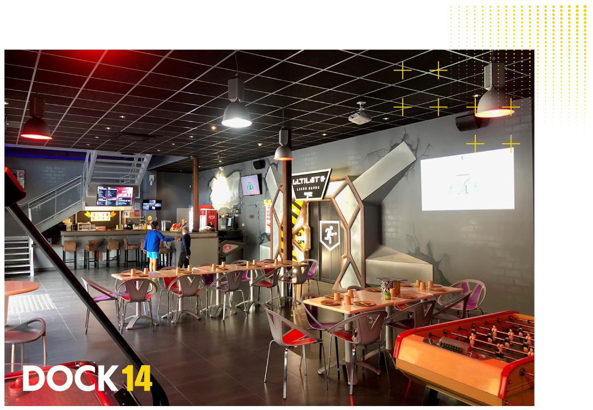 Vue d'ensemble de la salle du Dock 14 Laser Game à Echirolles Grenoble. Tables, casiers, écran géant, babyfoot et bar snacking.